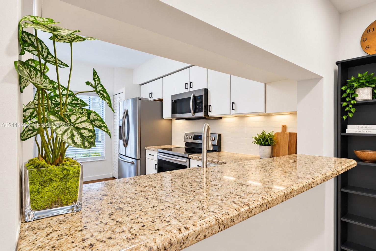 Pass-through kitchen counter with natural stone surface, white cabinetry, under-cabinet lighting, and stainless steel appliances