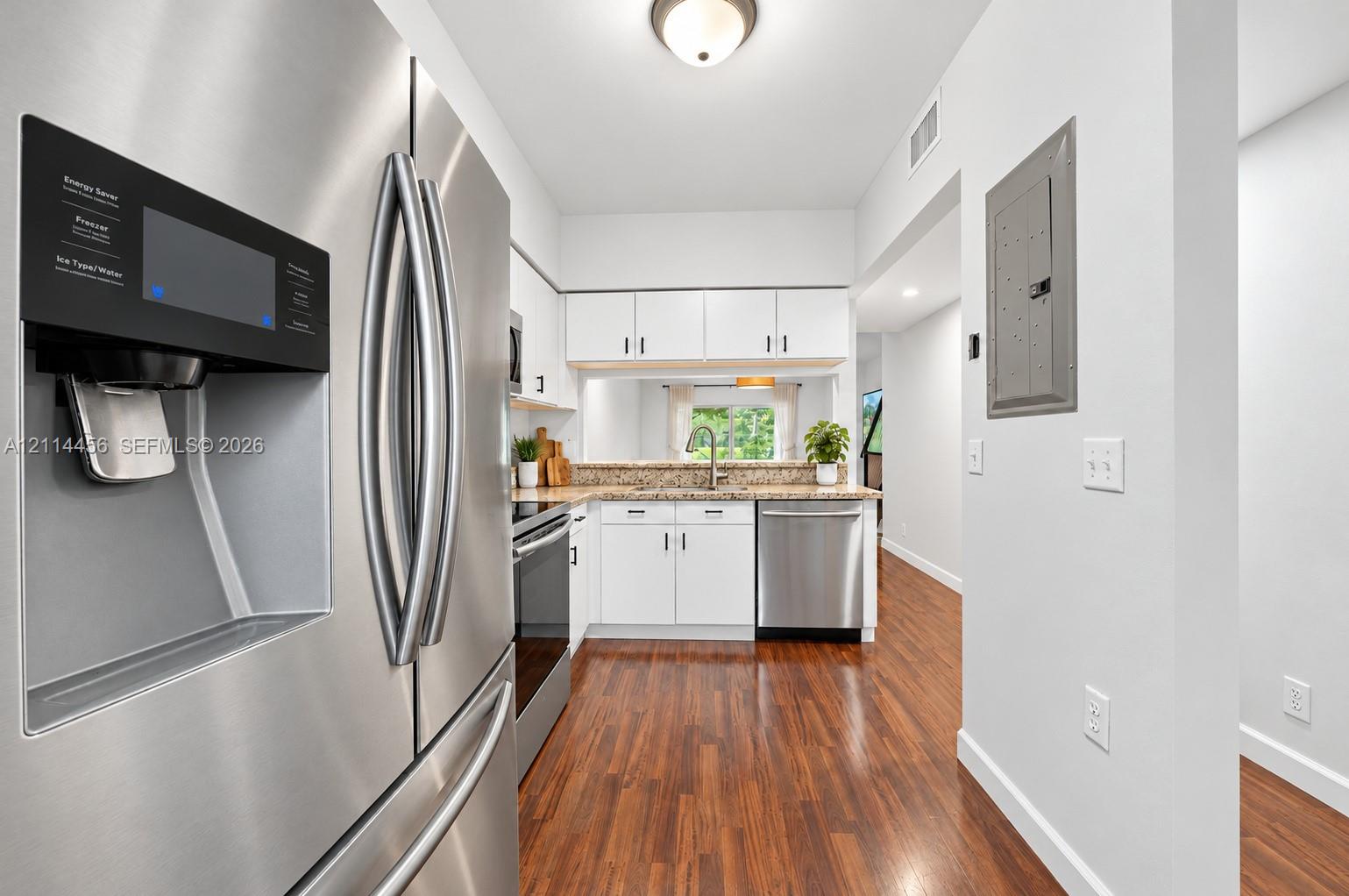 Kitchen featuring stainless steel appliances, white cabinetry, stone-finish countertops, and wood-finish flooring