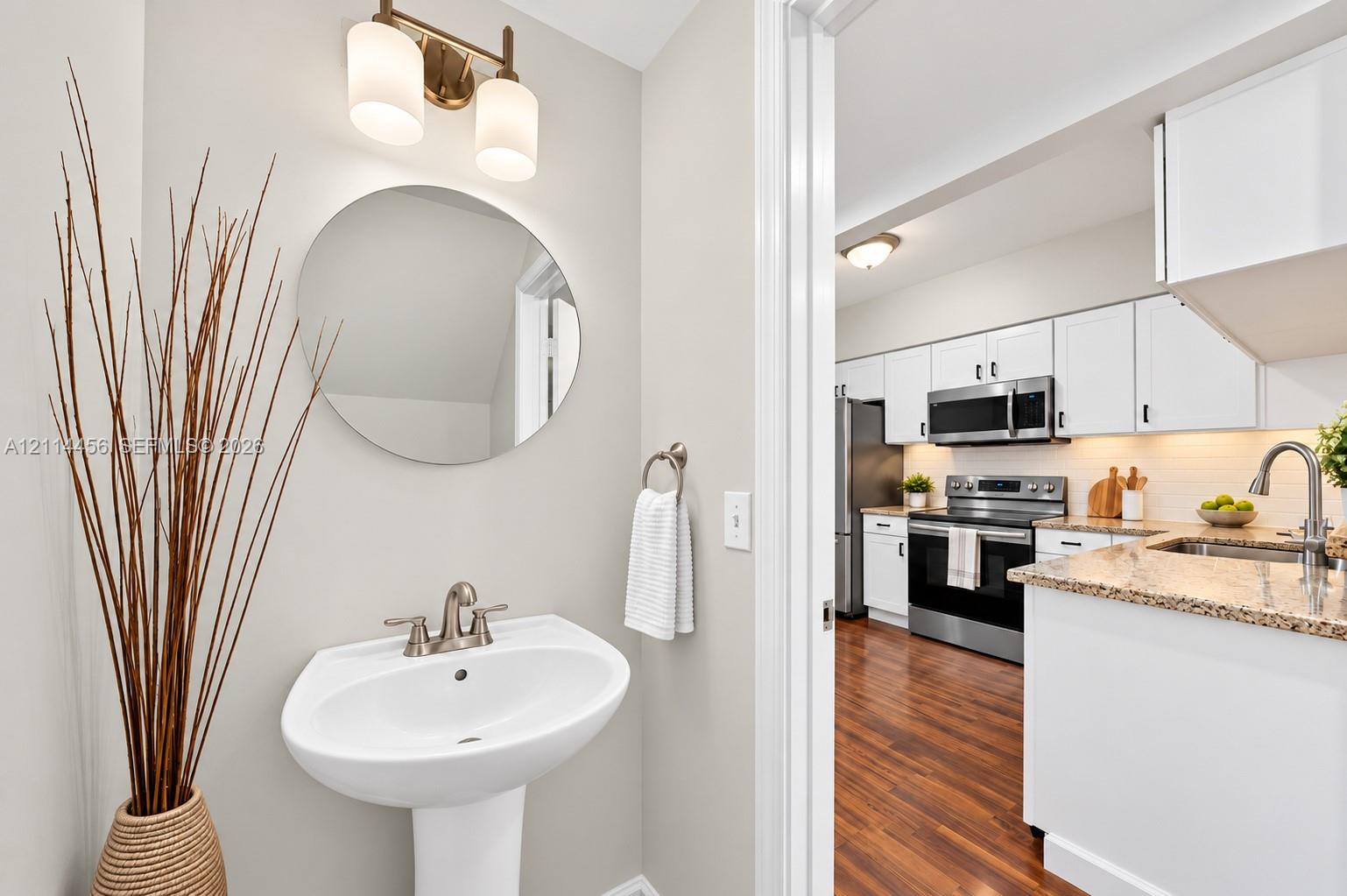Powder room featuring a white pedestal sink, circular mirror, and brushed-nickel wall-mounted light fixture