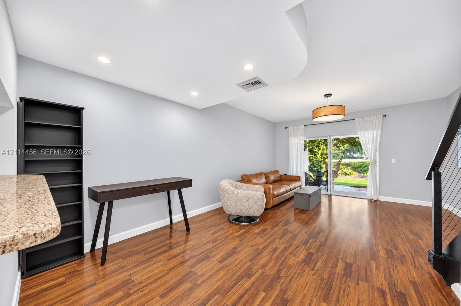 Wood-finish flooring, recessed lighting, curved architectural ceiling detail, drum-style chandelier, and sliding glass doors with exterior access