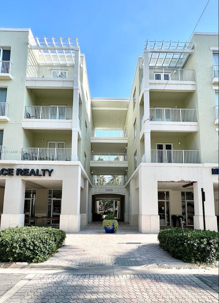 Multi-story mixed-use building featuring stucco exterior, private balconies with metal railings, top-level pergolas, and a paved pedestrian thoroughfare Multi-story mixed-use building featuring stucco exterior, private balconies with metal railings, top-level pergolas, and a paved pedestrian thoroughfare