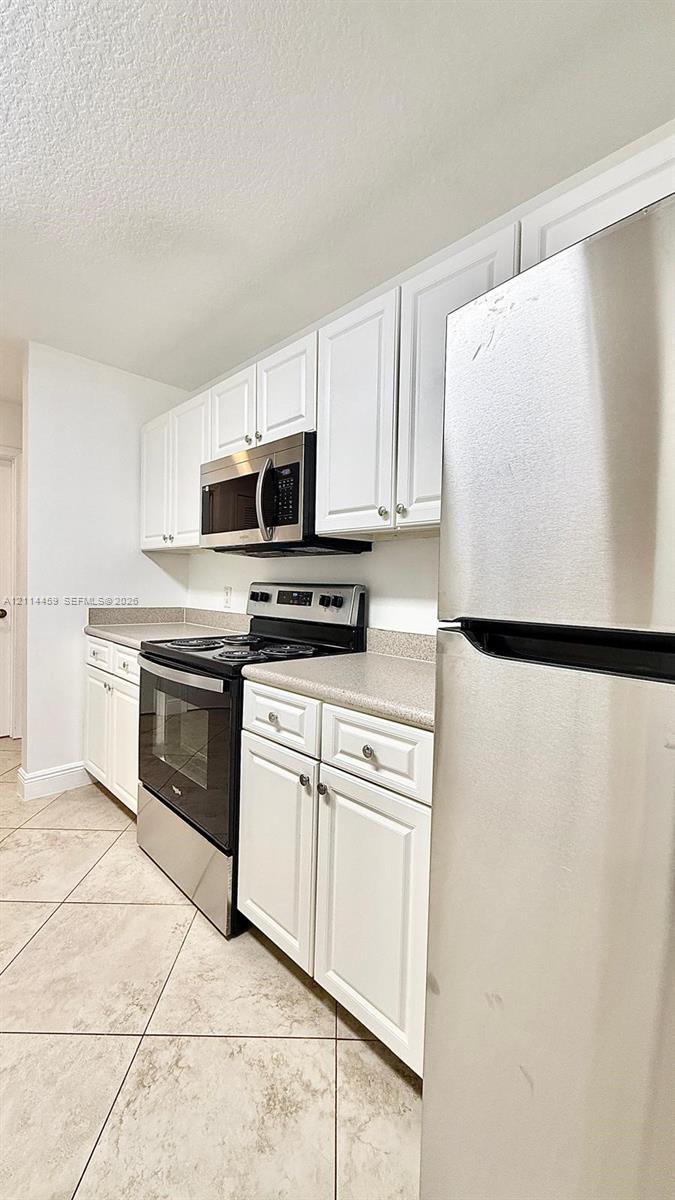 Kitchen featuring white cabinetry, solid-surface countertops, stainless steel appliances, and tile flooring
