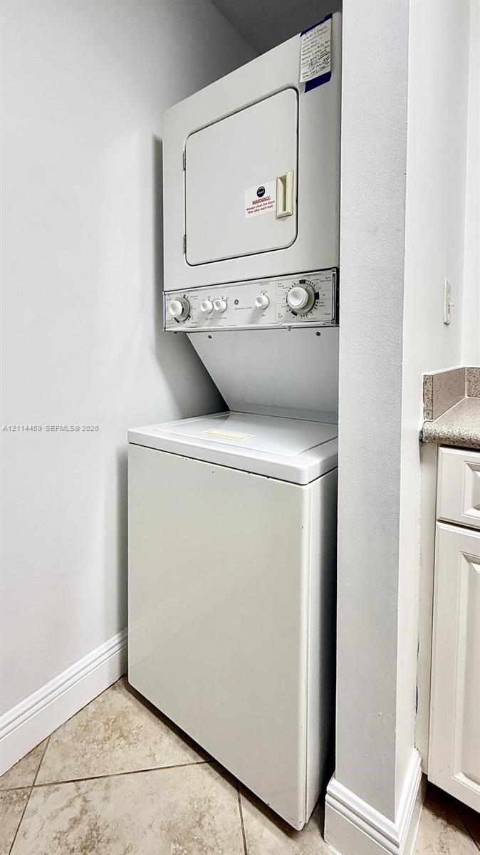 Stacked laundry unit featuring a top-load washer, a front-load dryer, and natural stone-finish floor tiling