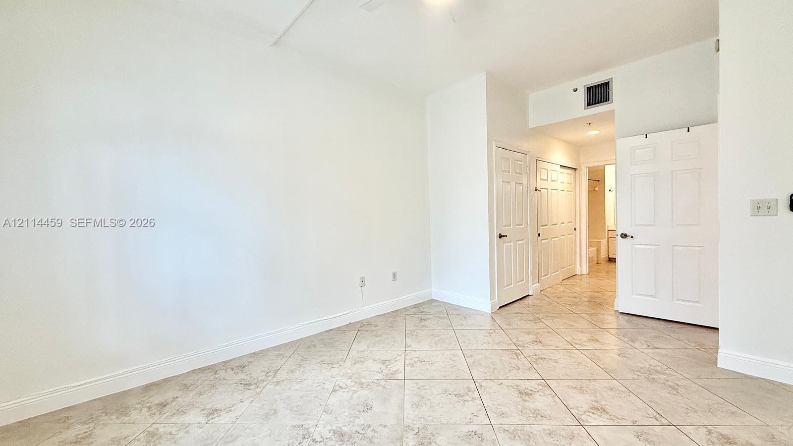 Neutral-toned ceramic tile flooring, three white six-panel interior doors, and a ceiling-mounted light fixture