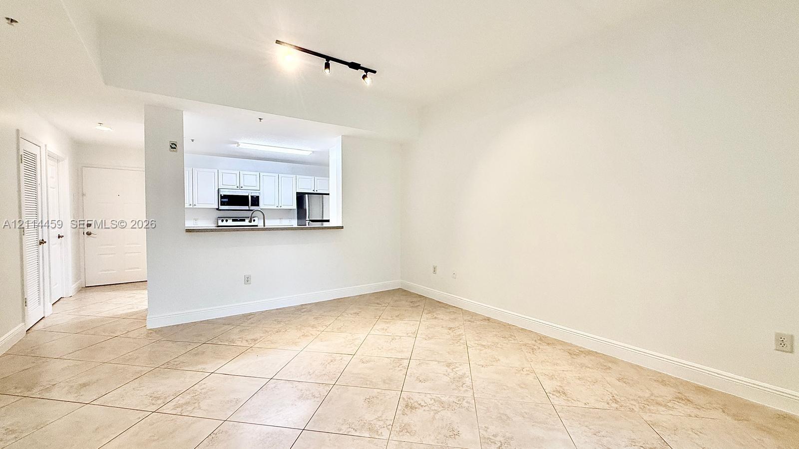 Open-concept interior featuring large-format ceramic tile flooring, neutral wall finishes, track lighting, and a breakfast bar pass-through to the kitchen area