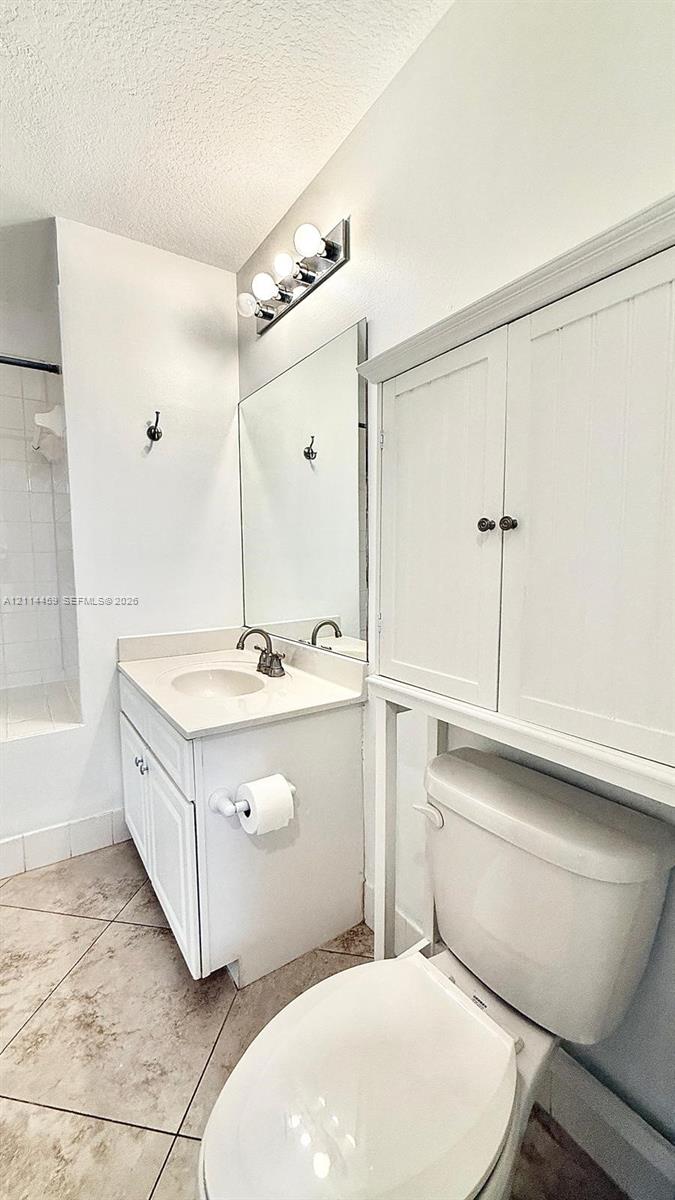Bathroom featuring a white vanity with a neutral solid-surface countertop, an integrated sink, built-in over-toilet cabinetry, a large wall mirror, and tile flooring