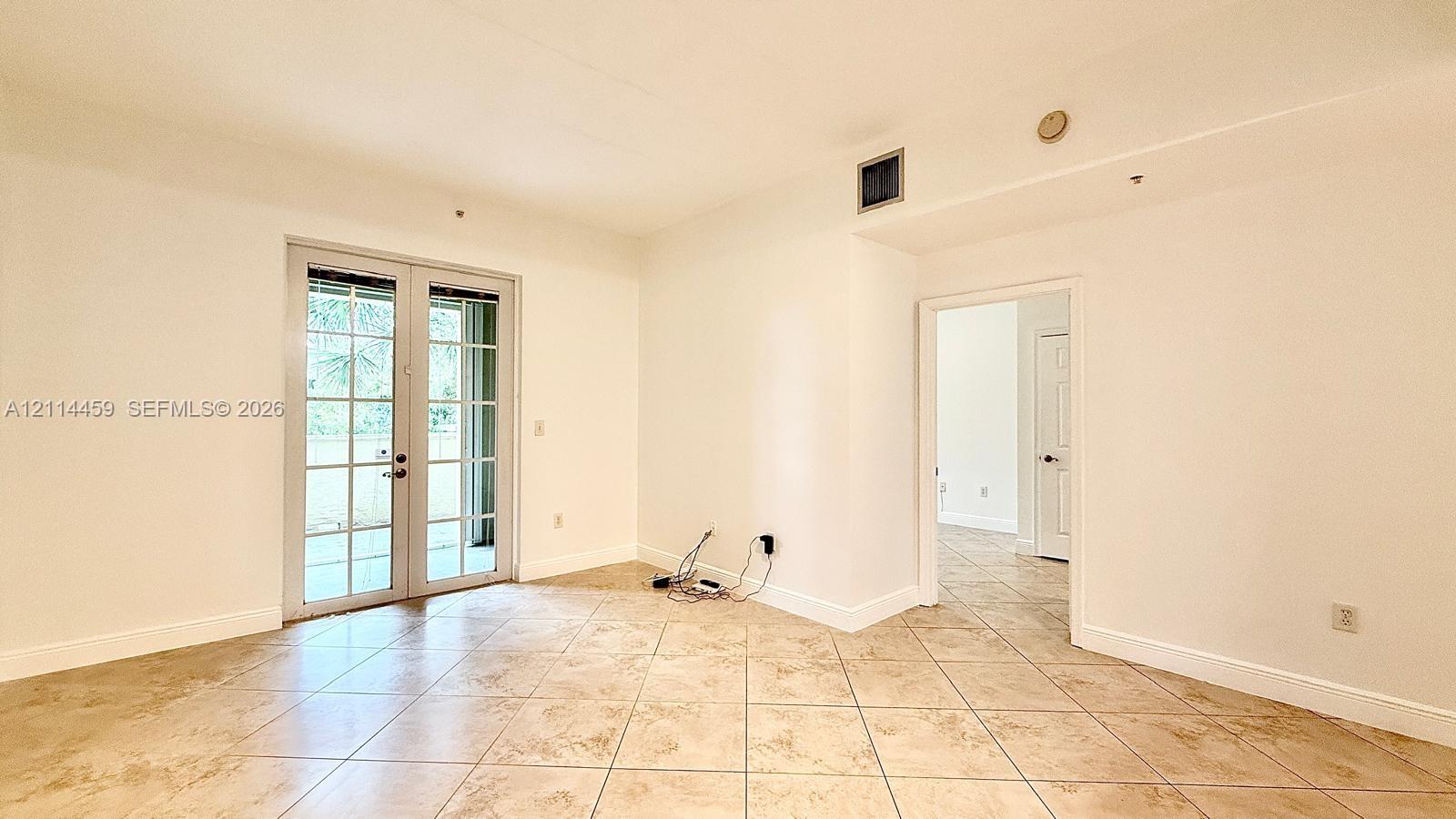 Neutral interior space featuring ceramic tile flooring, white walls, and glass-paneled double doors
