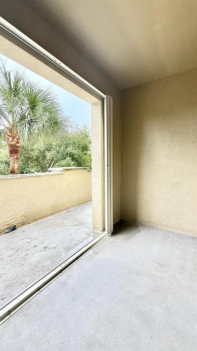Covered balcony featuring concrete flooring, textured walls, and a glass-paneled sliding door
