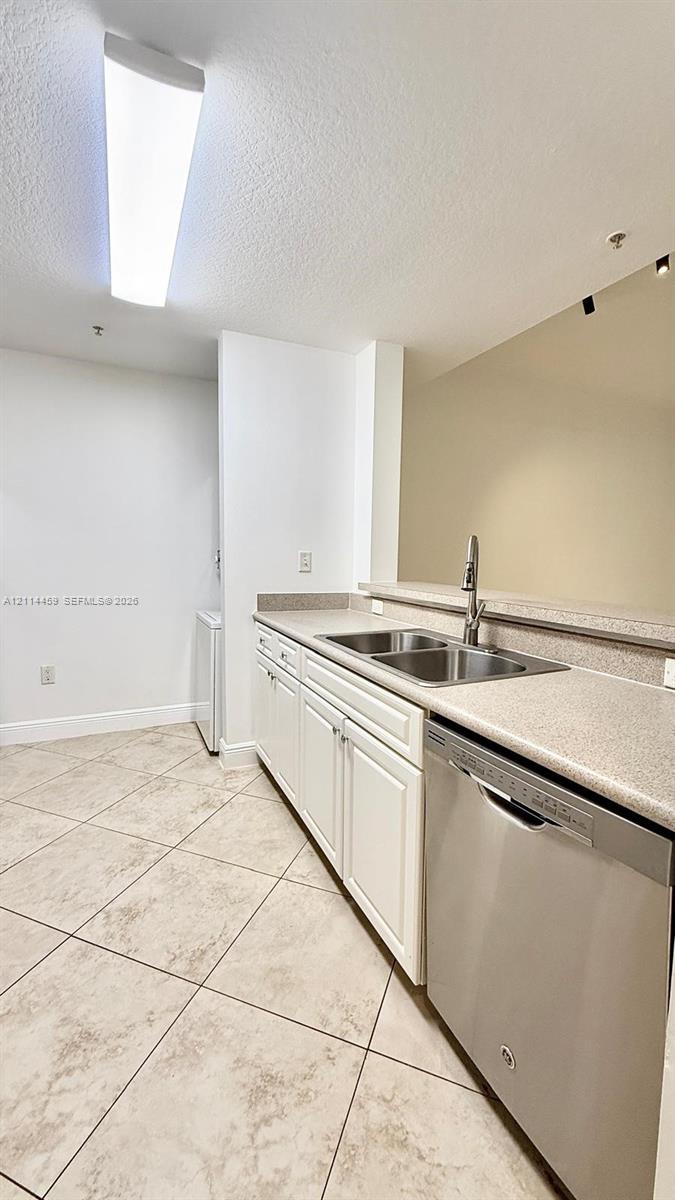 Kitchen featuring solid-surface countertops, dual-basin stainless steel sink with a high-arc faucet, stainless steel dishwasher, white cabinetry, and tile flooring