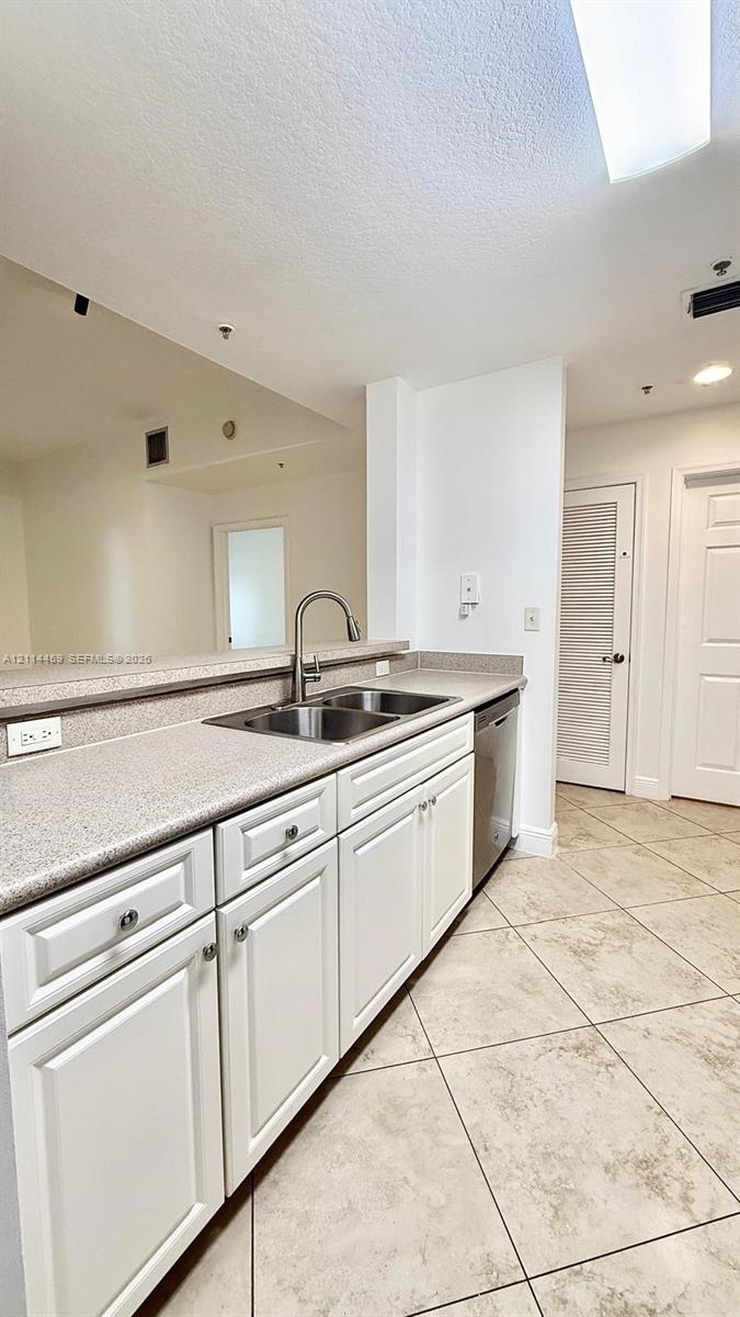 Kitchen featuring white shaker-style cabinetry, solid-surface countertops, dual-basin stainless steel sink with high-arc faucet, stainless steel dishwasher, and diagonal-set tile flooring