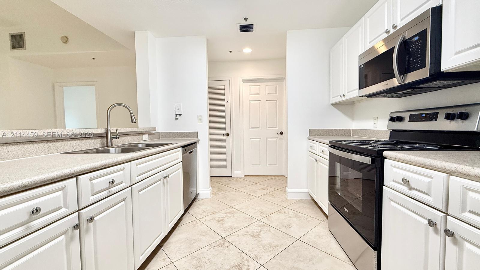 Kitchen featuring white cabinetry, stone-finish countertops, stainless steel appliances, a double-basin sink, and tile flooring