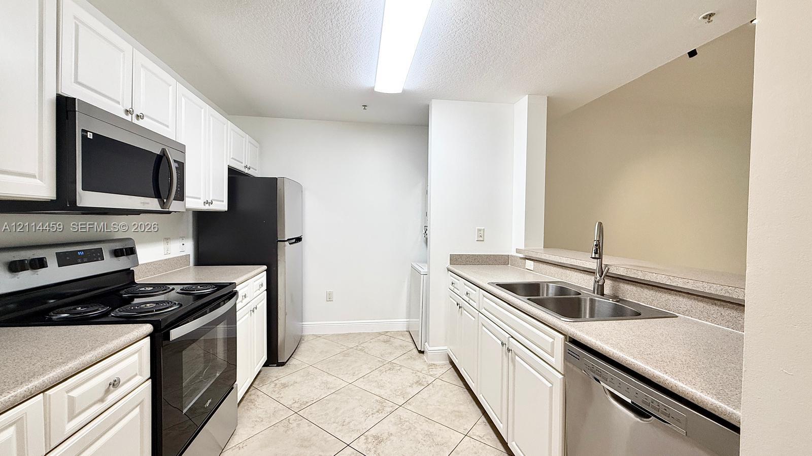 Kitchen featuring white cabinetry, solid surface countertops, a dual-basin stainless steel sink, tile flooring, and stainless steel appliances