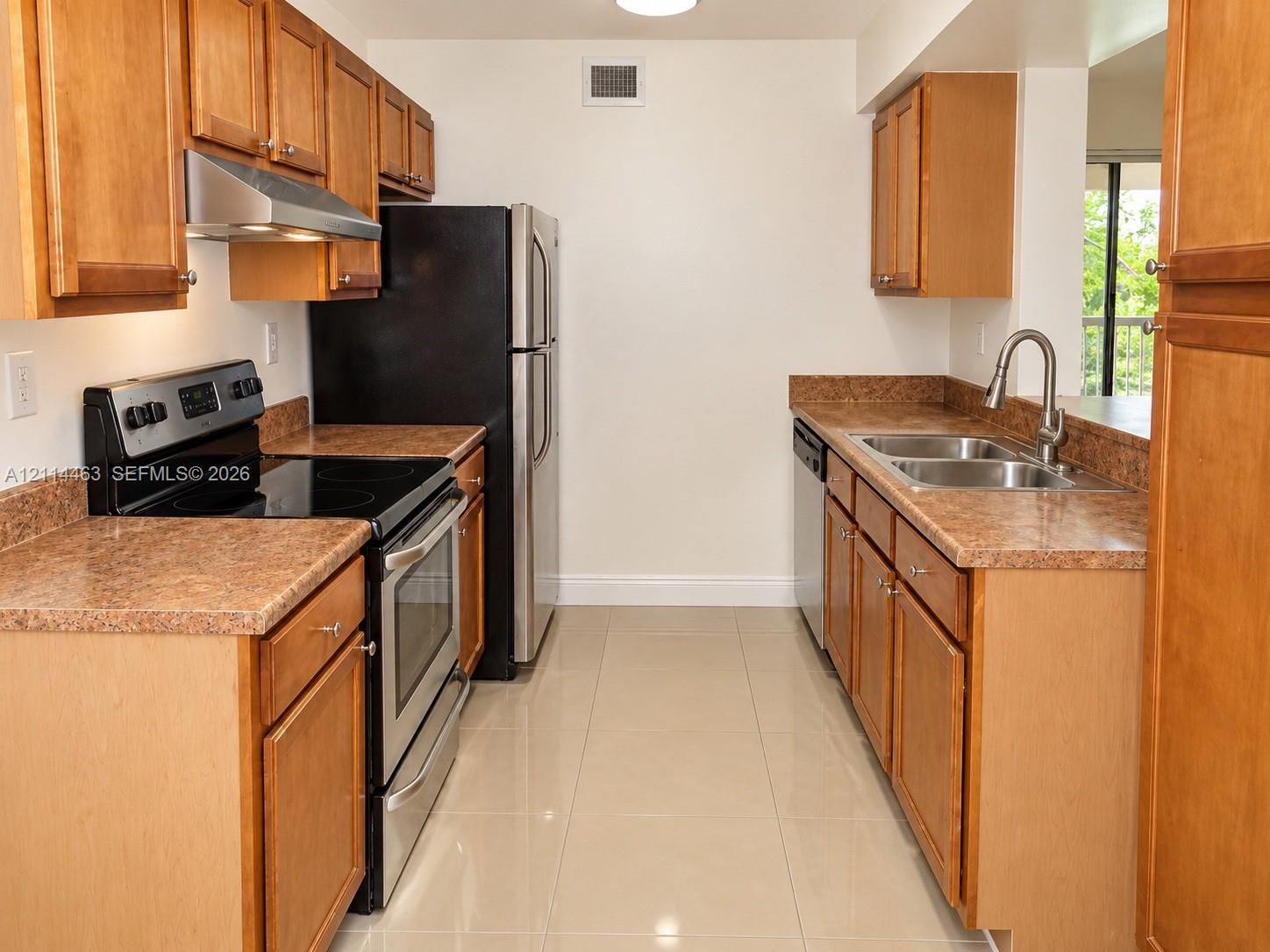 Kitchen featuring natural wood-finish cabinetry, stone-texture countertops, stainless steel appliances, a double-basin sink with a gooseneck faucet, and tile flooring Kitchen featuring natural wood-finish cabinetry, stone-texture countertops, stainless steel appliances, a double-basin sink with a gooseneck faucet, and tile flooring