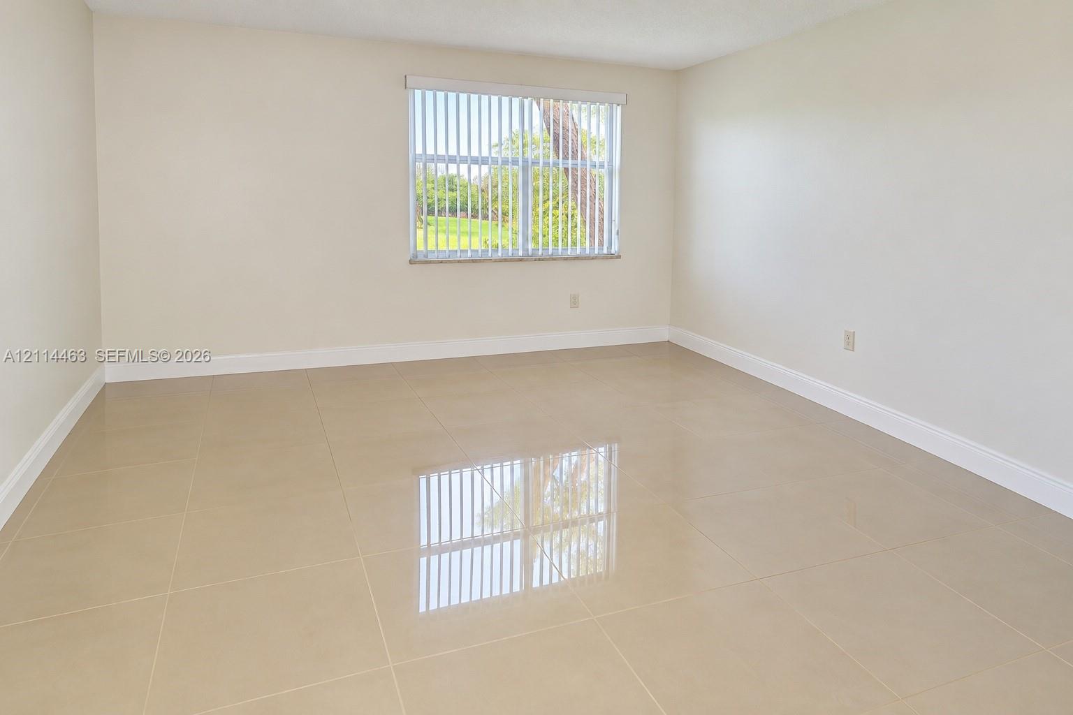 Neutral-toned interior space featuring polished large-format tile flooring, smooth wall finishes, and a single window with vertical blinds Neutral-toned interior space featuring polished large-format tile flooring, smooth wall finishes, and a single window with vertical blinds