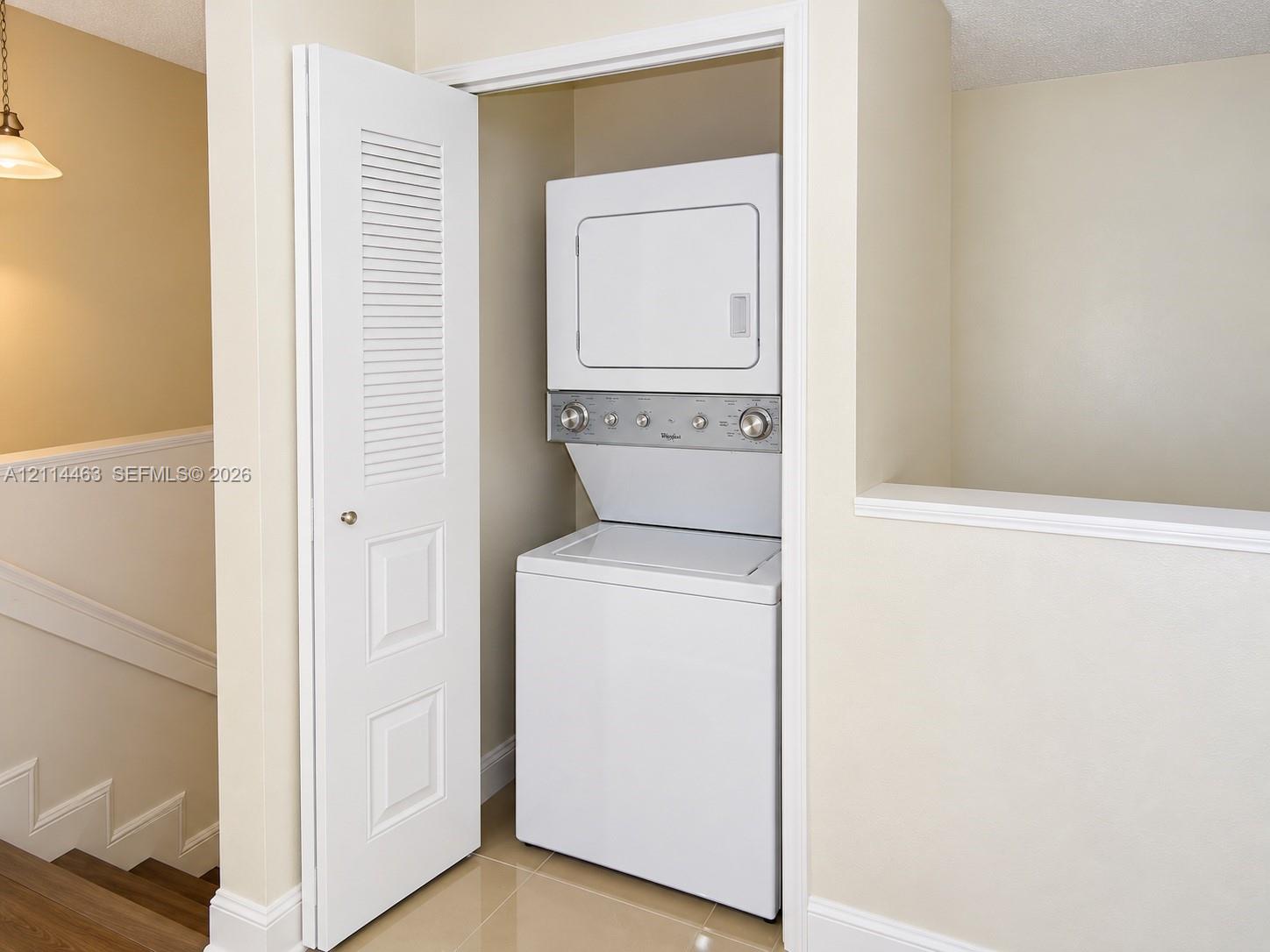 Laundry closet featuring a white stacked washer and dryer unit and a white louvered panel door Laundry closet featuring a white stacked washer and dryer unit and a white louvered panel door