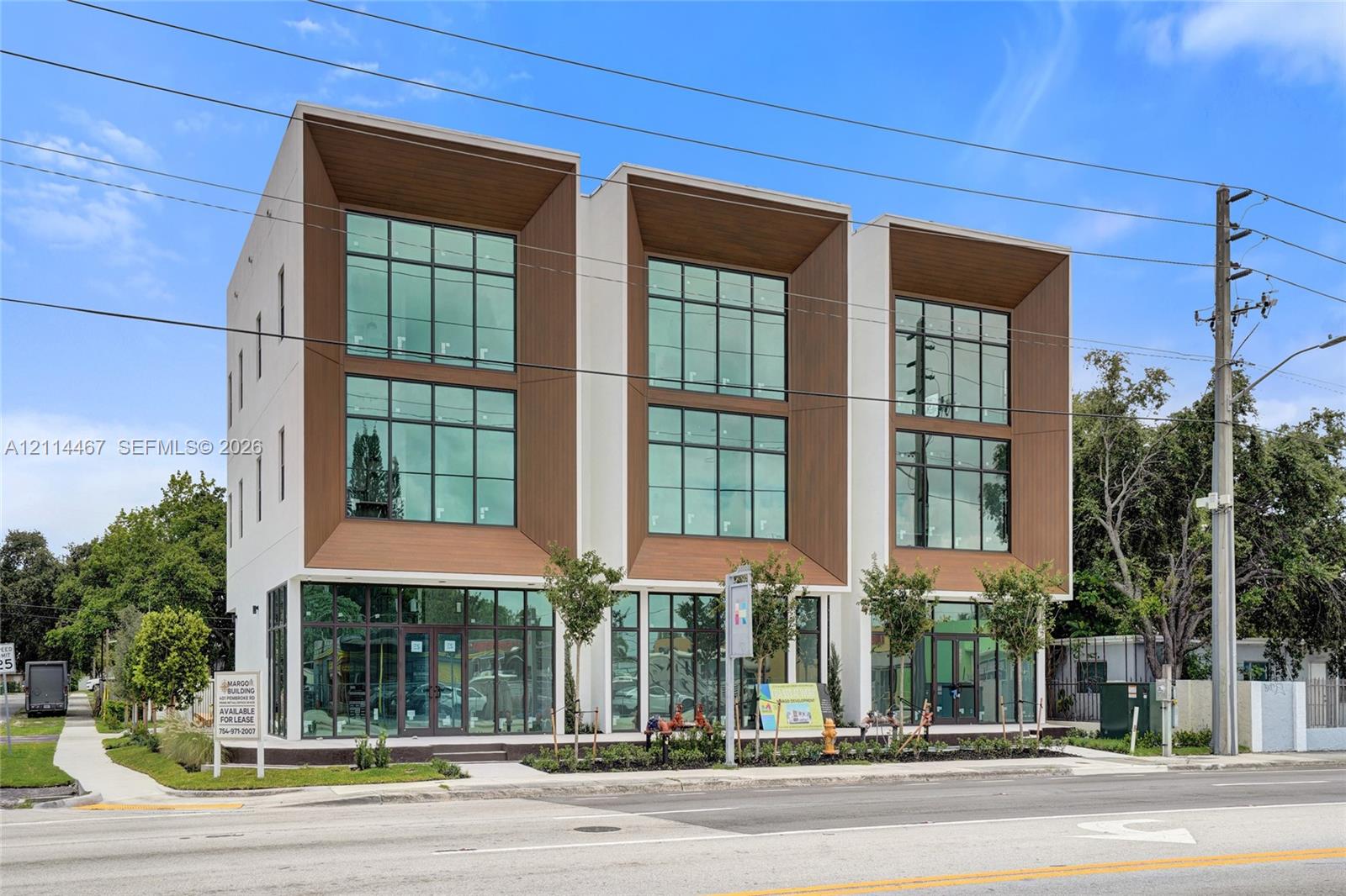 Three-story mixed-use building featuring a smooth stucco finish, floor-to-ceiling glass paneling, recessed timber-clad bays, and ground-level storefront glazing