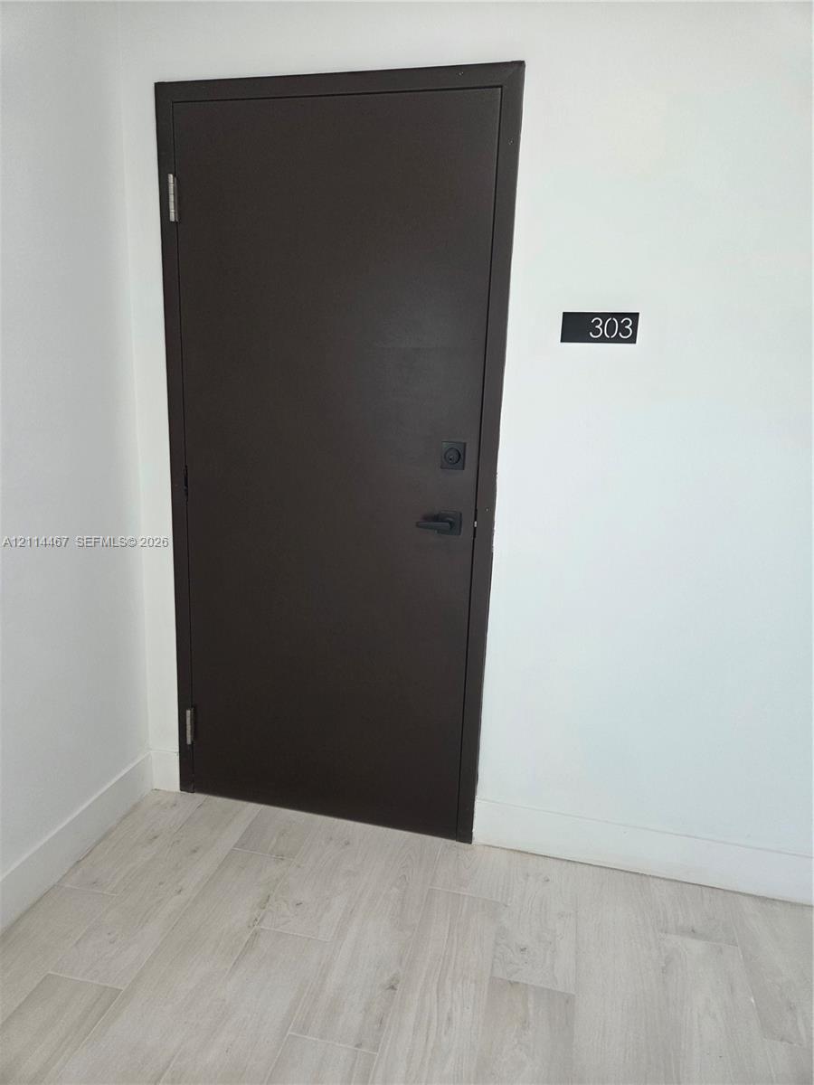 Solid dark-toned door with matte black hardware, featuring a modern numerical door plaque and light wood-finish flooring