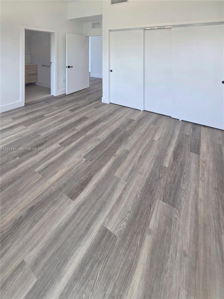 Interior room featuring wood-finish flooring, white walls, sliding closet doors, and solid-core passage doors