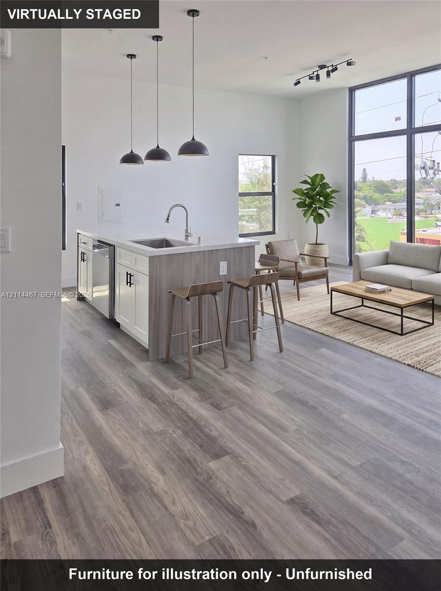 Kitchen featuring wood-finish flooring, a quartz-topped island with under-mount sink, three dome pendant lights, and floor-to-ceiling windows
