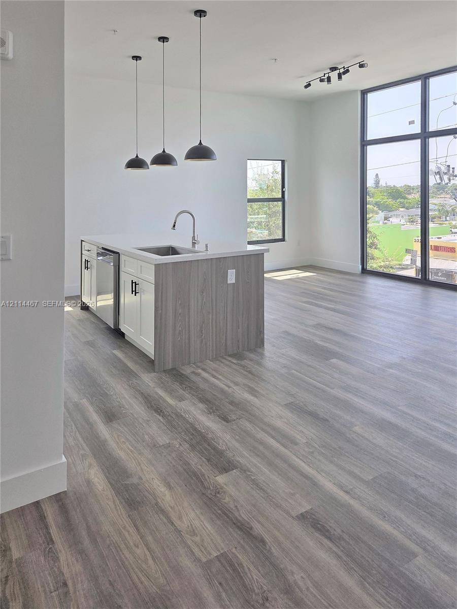 Kitchen island featuring two-tone cabinetry and stone countertops, complemented by wood-finish flooring, floor-to-ceiling windows, and matte black pendant lighting