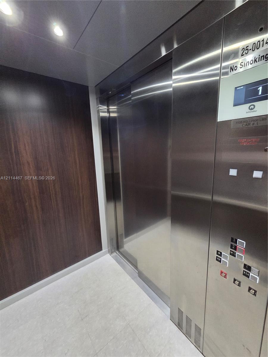 Elevator cab featuring stainless steel doors and control panel, wood-finish wall paneling, and recessed ceiling lighting