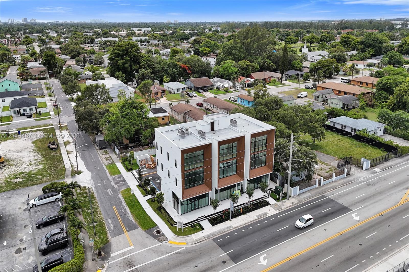Modern three-story multi-unit structure featuring a white facade, wood-tone recessed accents, floor-to-ceiling glass windows, and a flat roofline