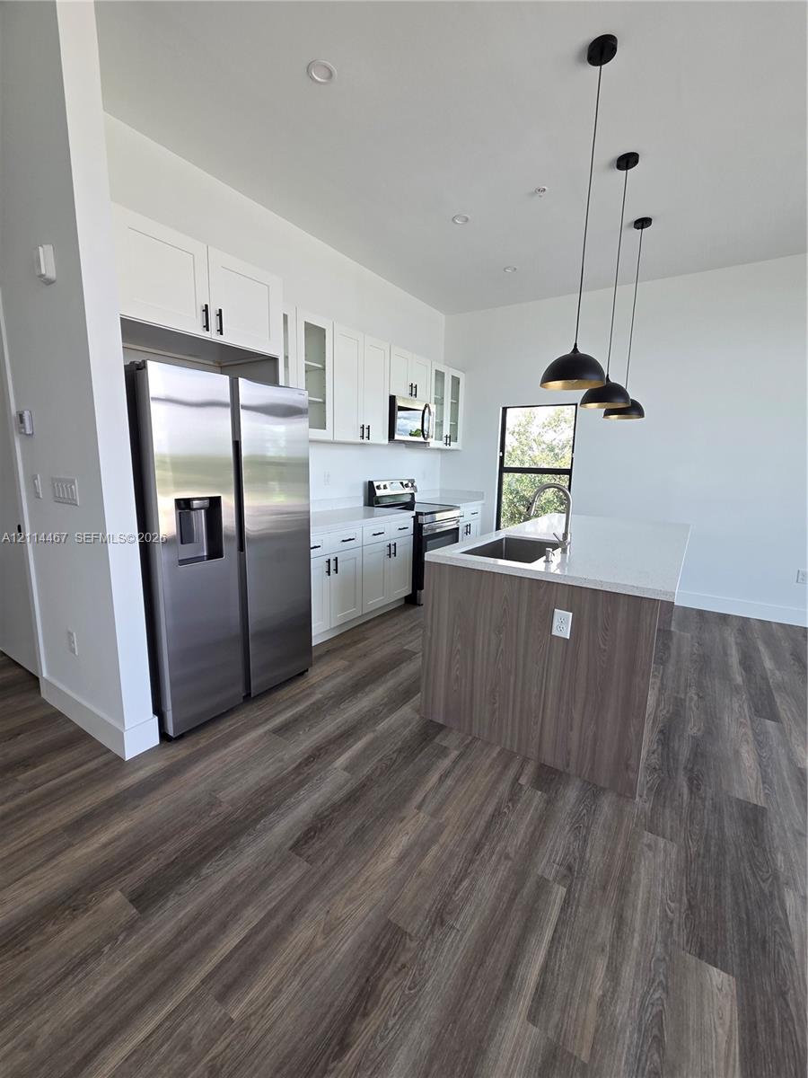 Kitchen featuring white cabinetry, quartz countertops, a central island with wood-finish paneling, stainless steel appliances, and matte black pendant lighting over wood-finish flooring