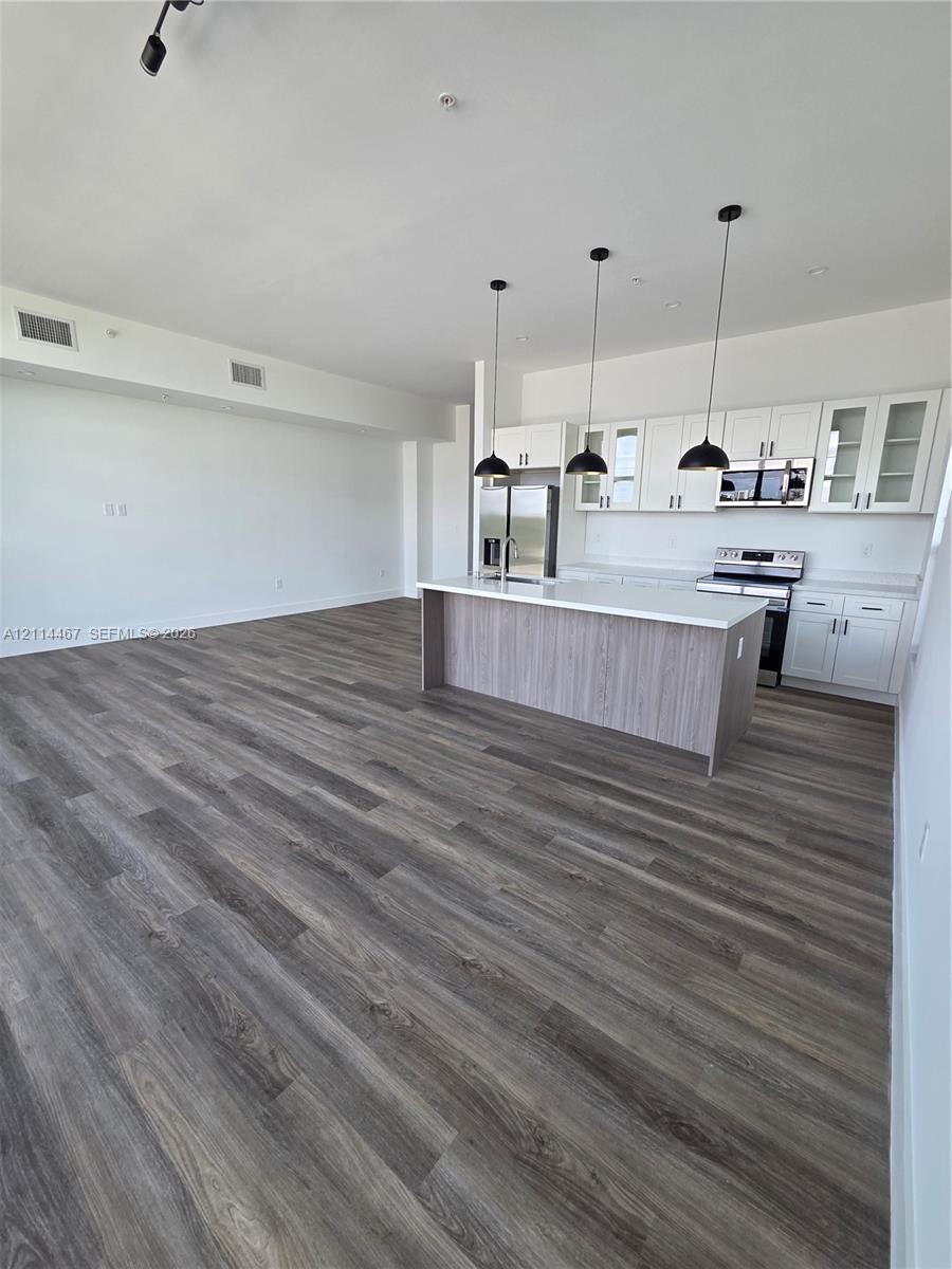 Kitchen featuring white cabinetry, wood-finish island with stone countertop, stainless steel appliances, and three pendant lights over wood-finish flooring