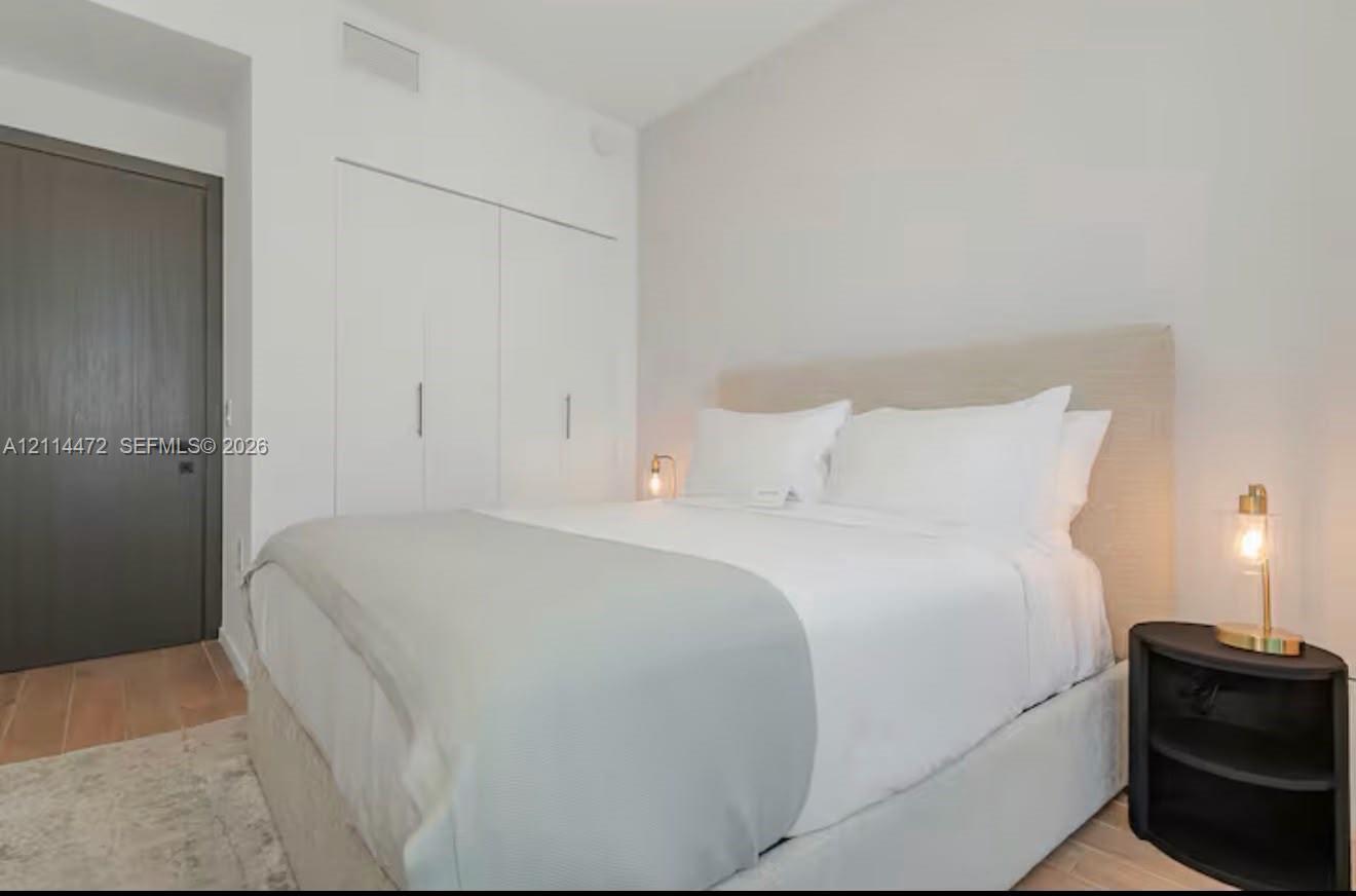 Wood-finish flooring, neutral walls, integrated full-height storage cabinetry with metallic hardware, and a solid-core charcoal interior door