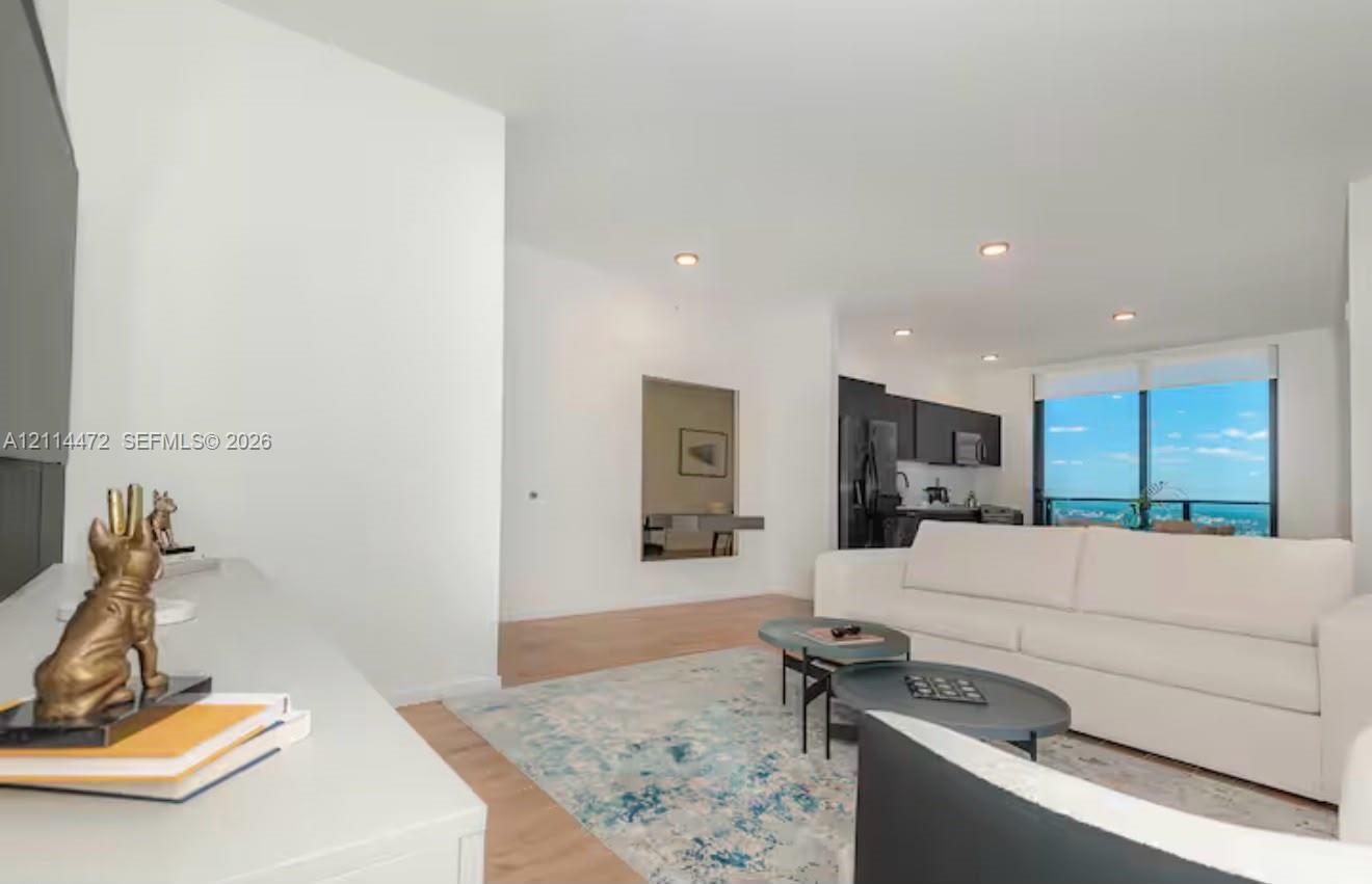 Open-concept interior featuring light wood-finish flooring, recessed lighting, and floor-to-ceiling windows with a distant skyline horizon