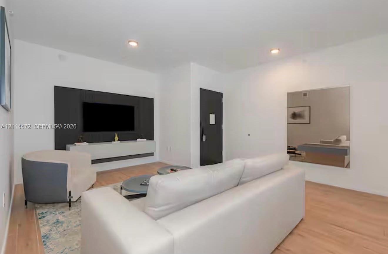 Wood-finish flooring, matte black entry door, wall-mounted floating media console, and recessed lighting