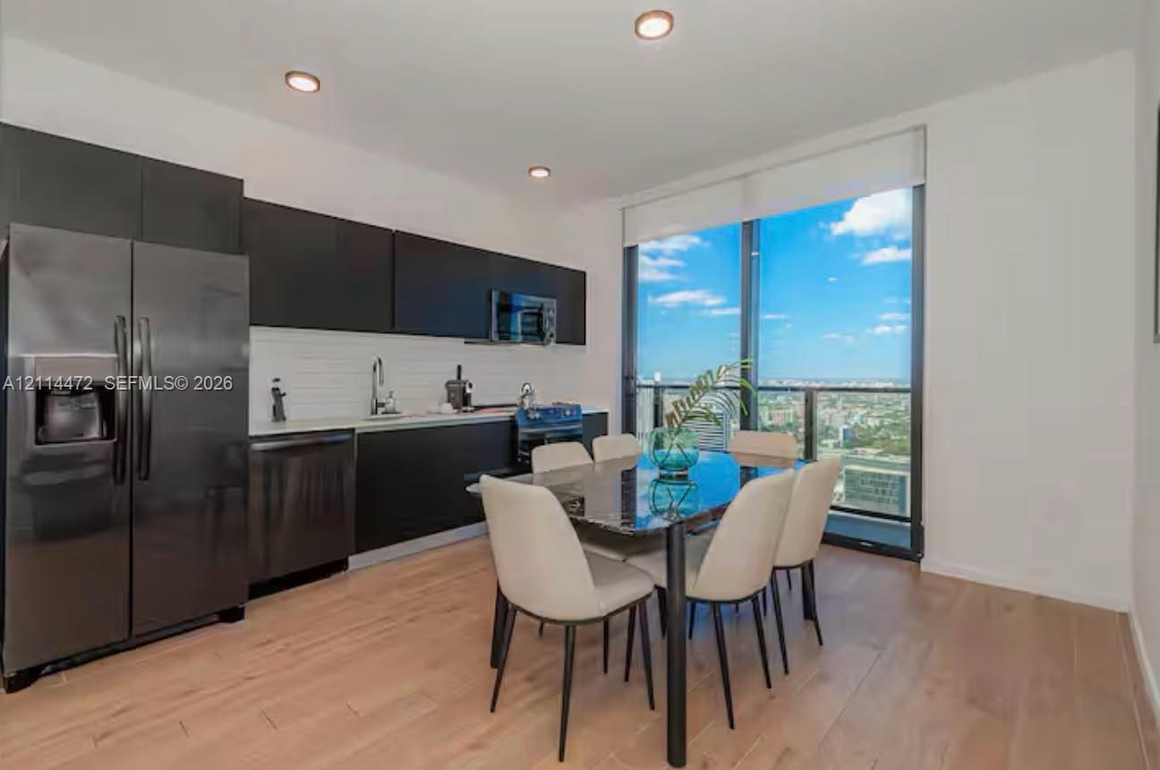 Modern kitchen featuring matte black flat-panel cabinetry, white horizontal tile backsplash, stainless steel appliances, wood-finish flooring, and floor-to-ceiling windows