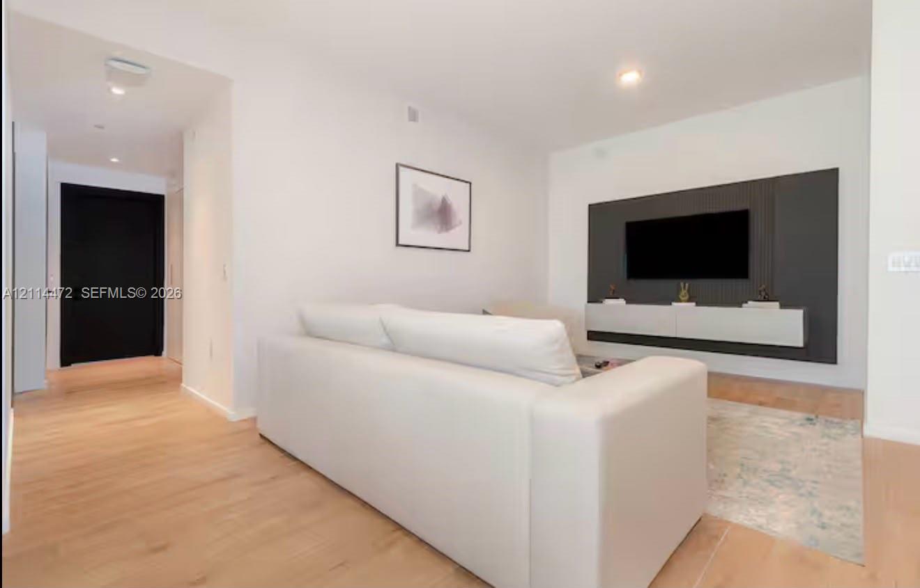 Living area featuring wood-finish flooring, a charcoal-toned paneled accent wall, a floating built-in console, and a solid black entry door