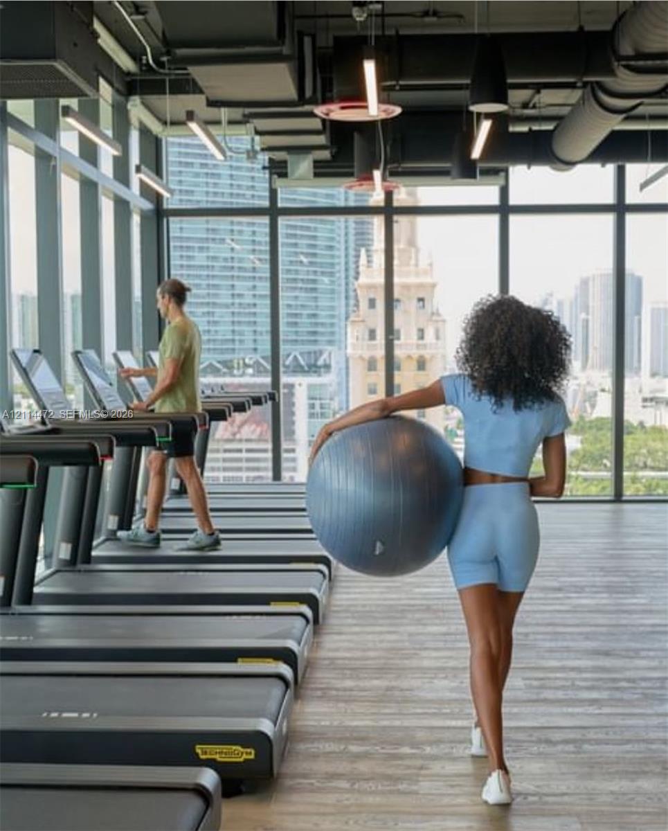 Fitness center featuring floor-to-ceiling windows, wood-finish flooring, exposed industrial-style ceiling, and linear LED lighting