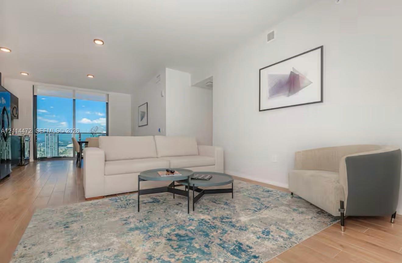 Open-concept living space featuring wood-finish flooring, recessed lighting, and floor-to-ceiling glass paneling with balcony access