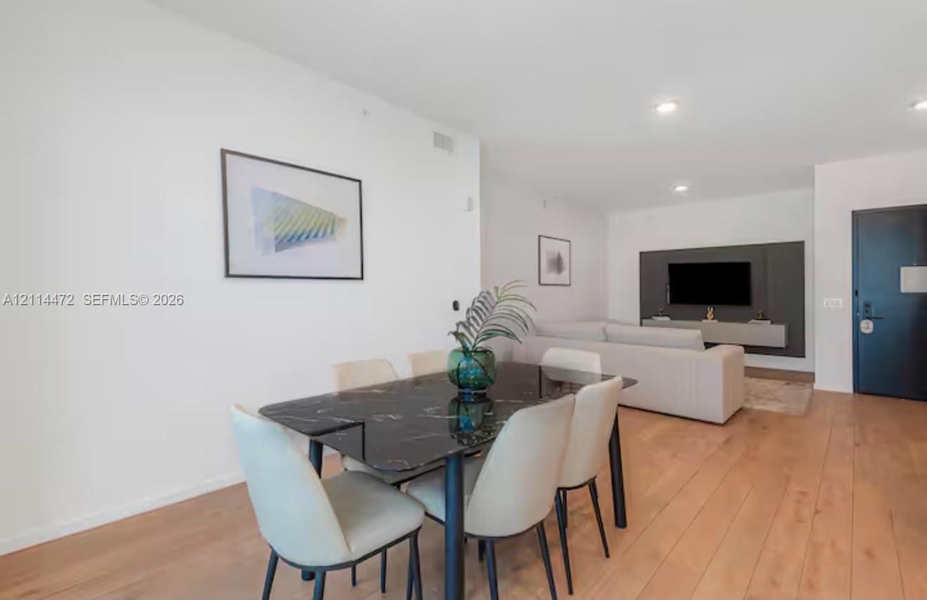 Open-concept interior featuring wood-finish flooring, recessed lighting, and a dark accent wall with a wall-mounted media console