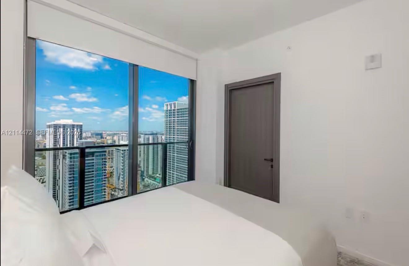 Floor-to-ceiling windows with dark metallic frames, panoramic cityscape, retractable roller shade, and solid-core door with matte black hardware