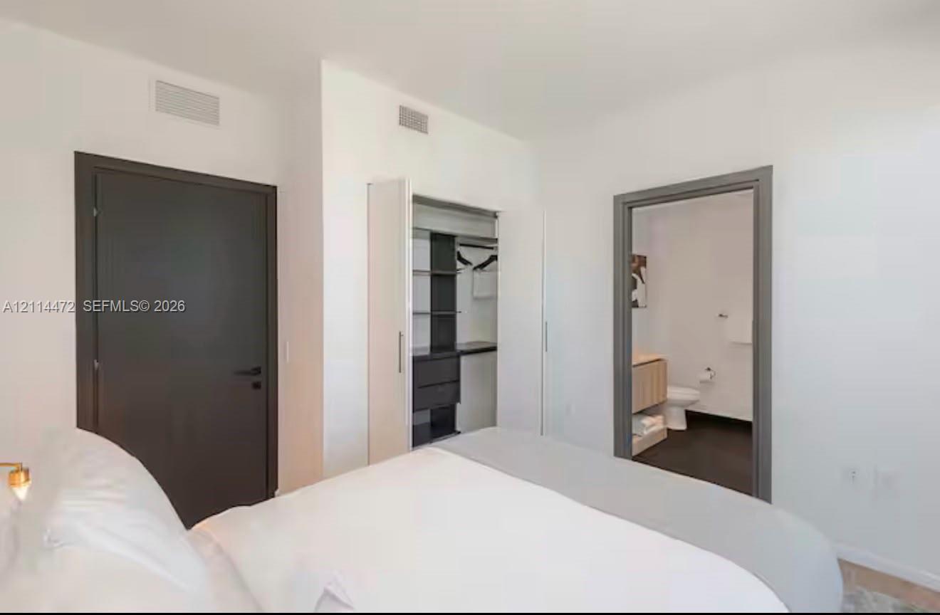 Neutral-toned bedroom featuring a dark solid-core door, built-in closet with integrated shelving, and a doorway showcasing a vanity with a light-finish cabinet