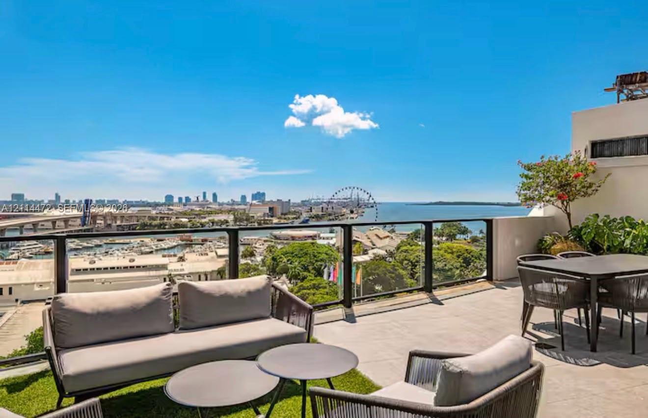 Elevated terrace with large-format tile flooring, perimeter glass railing, and panoramic water and city skyline backdrop