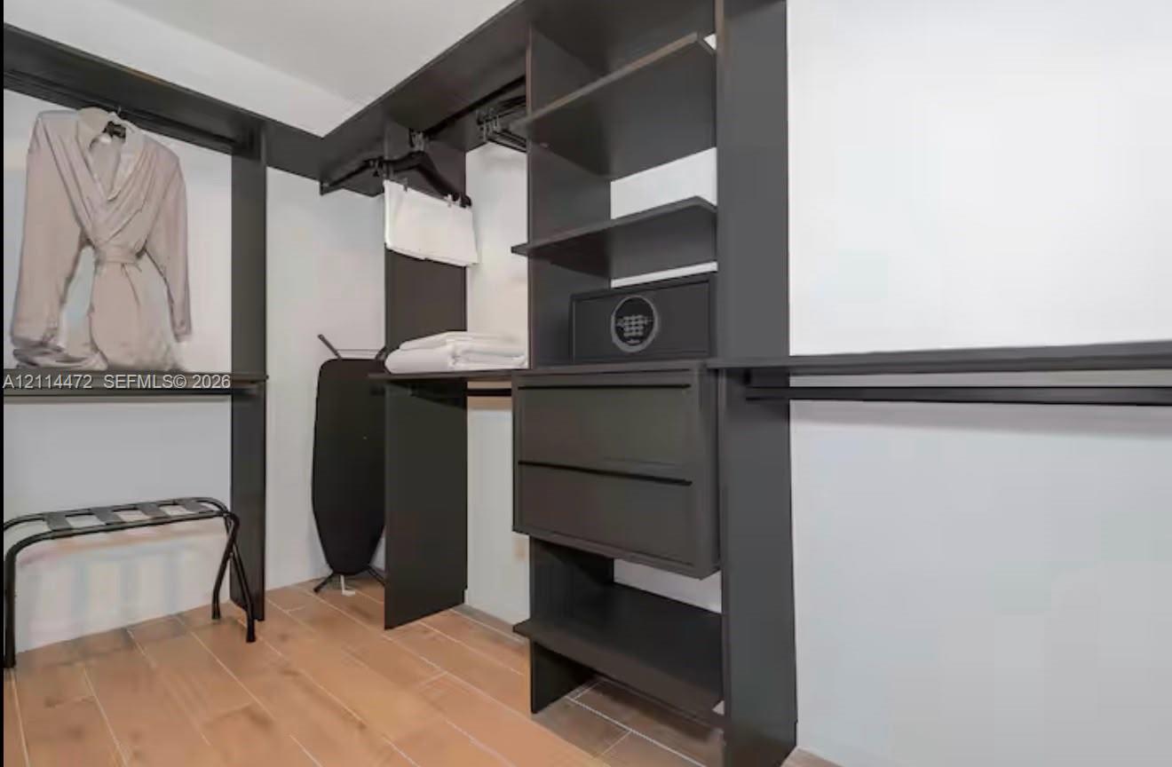 Walk-in closet featuring floor-to-ceiling dark-finish built-in cabinetry, multiple hanging rods, integrated drawer storage, and wood-finish flooring