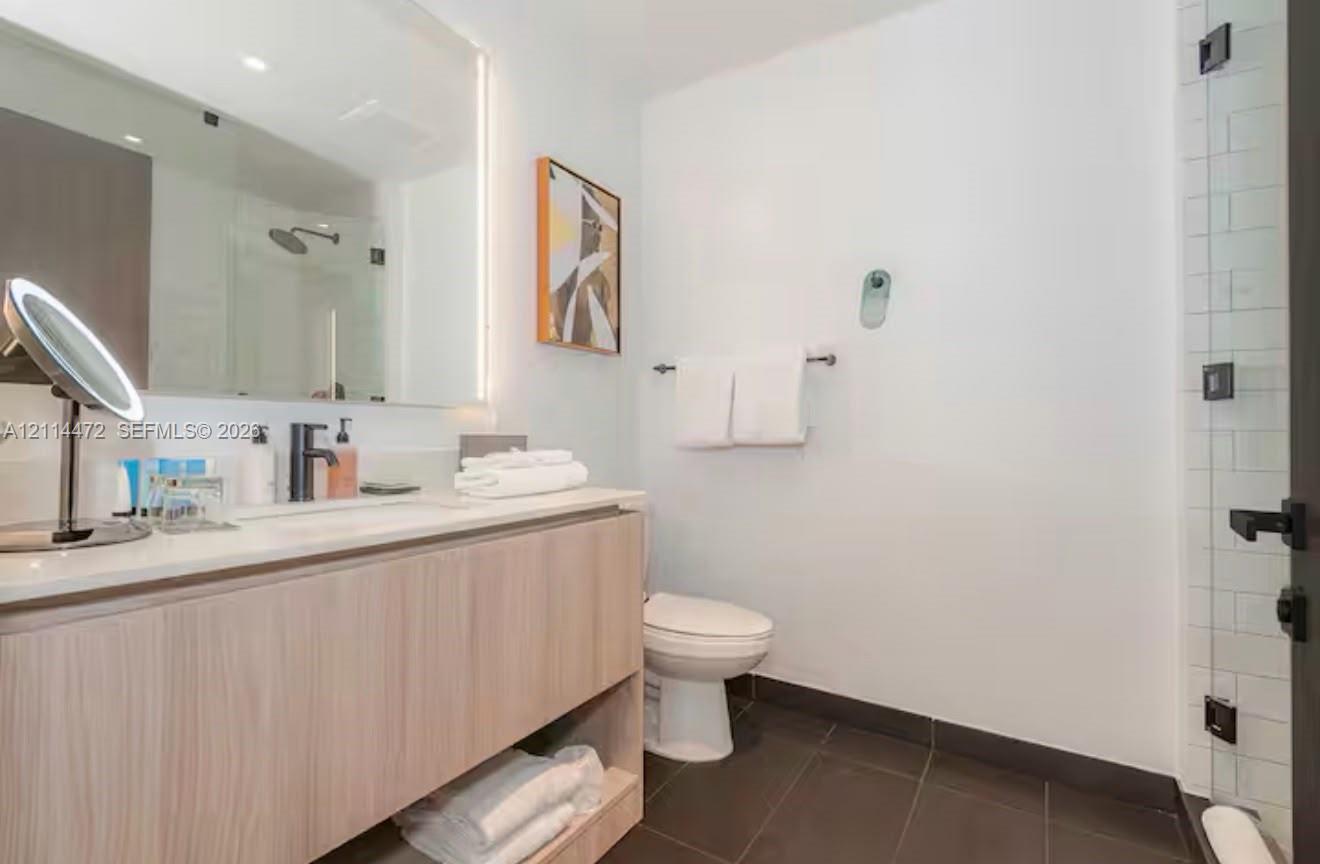 Floating wood-finish vanity with a rectangular sink, integrated LED mirror lighting, dark-toned floor tiling, and a glass-enclosed shower with subway tile surround