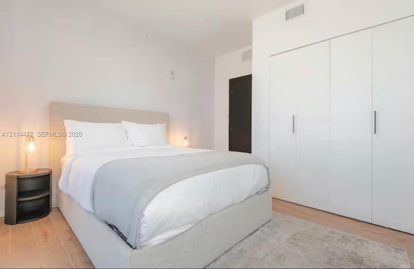 Room featuring smooth-finish white walls, light-toned wood-finish flooring, and built-in floor-to-ceiling storage cabinetry with vertical metallic hardware