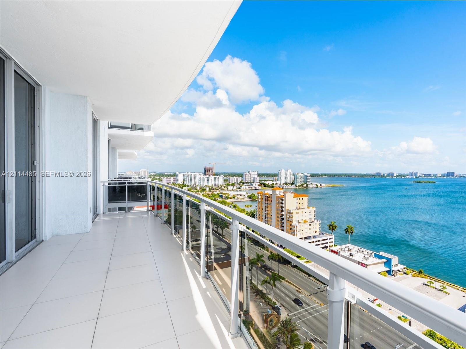 Covered balcony featuring tile flooring and a glass-paneled metal railing overlooking the waterfront