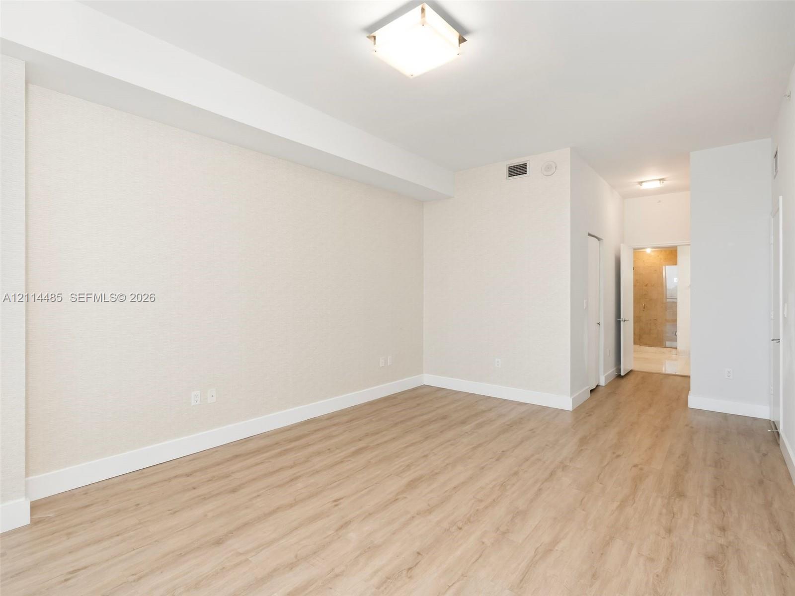 Neutral-toned interior space featuring wood-finish flooring, textured wall finishes, and a flush-mount square ceiling light fixture
