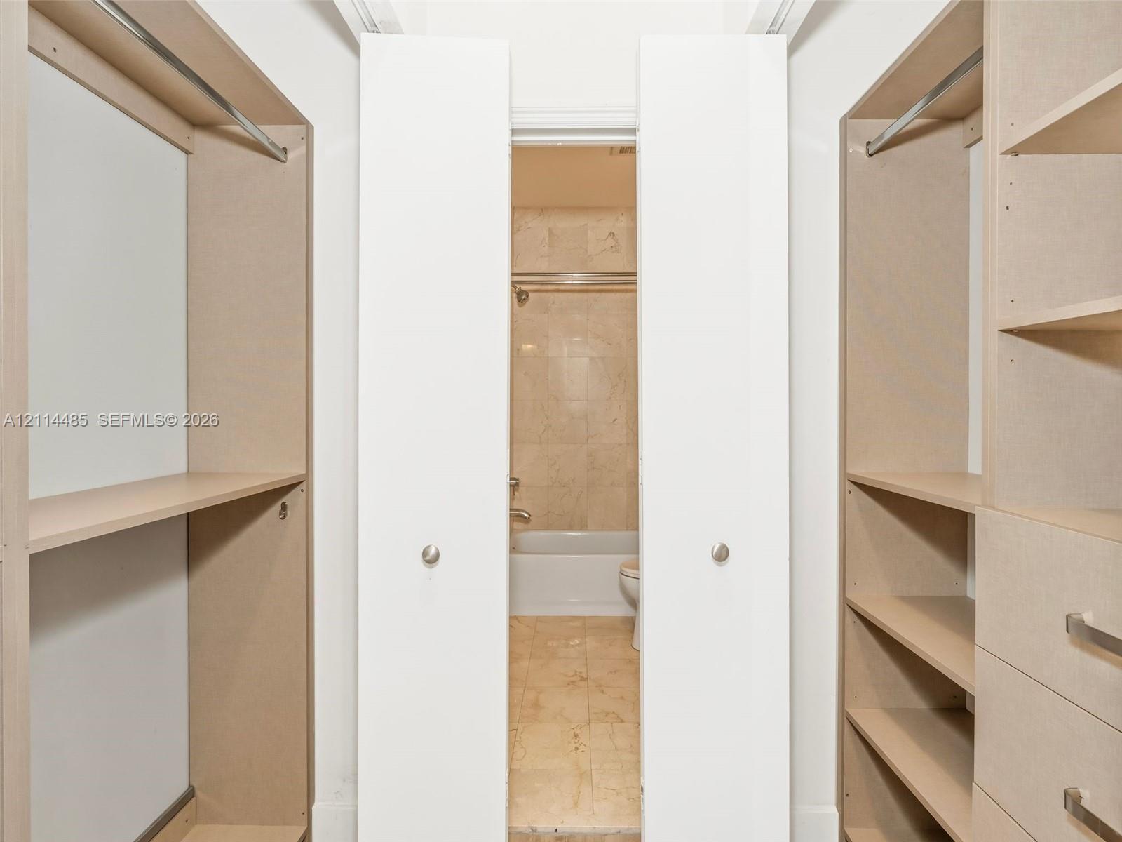 Custom reach-in closet featuring light wood-finish built-in shelving, integrated drawers with bar pulls, and metal garment rods