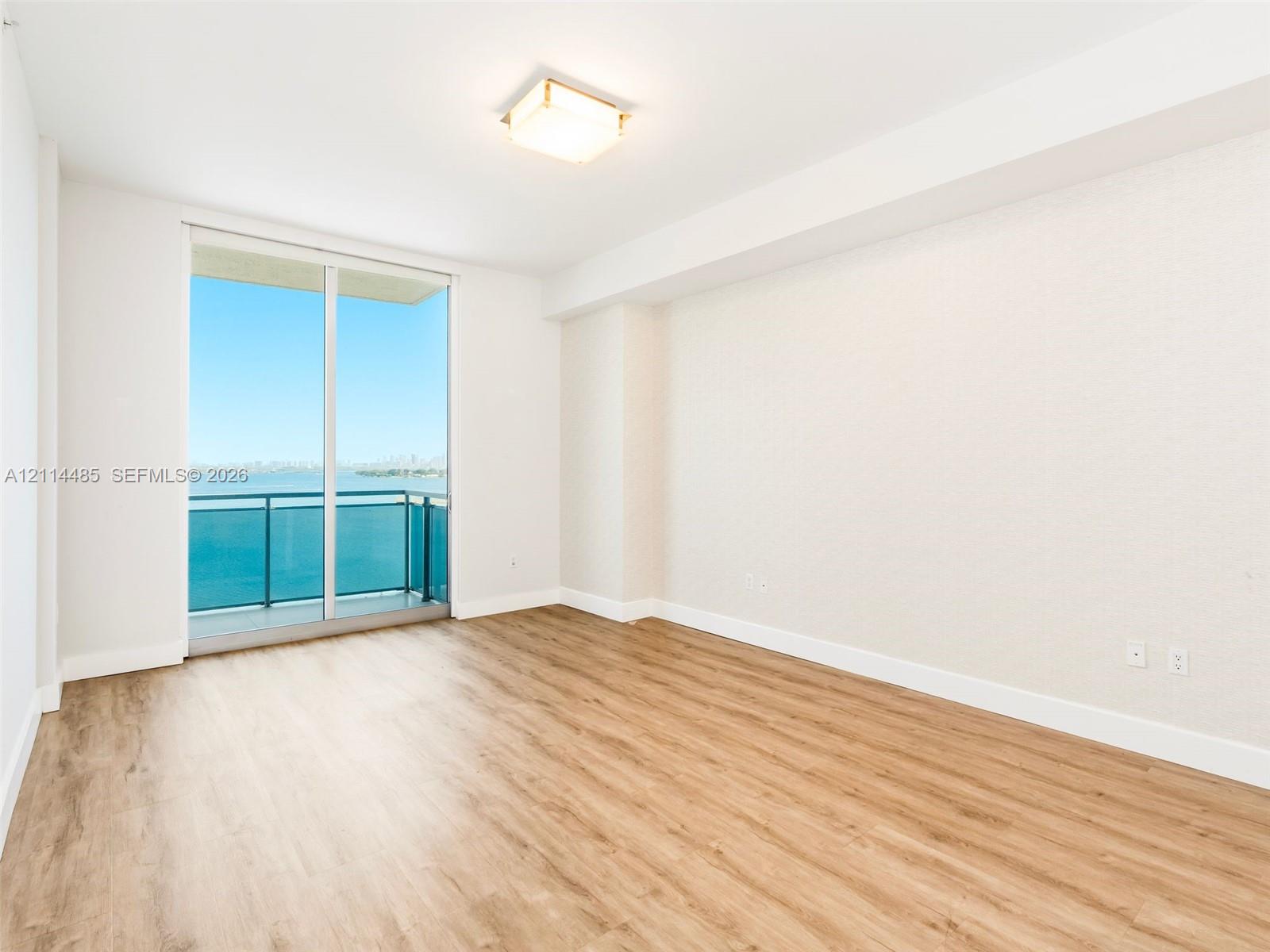 Floor-to-ceiling glass sliding doors with access to a private balcony, wood-finish flooring, and recessed ceiling lighting
