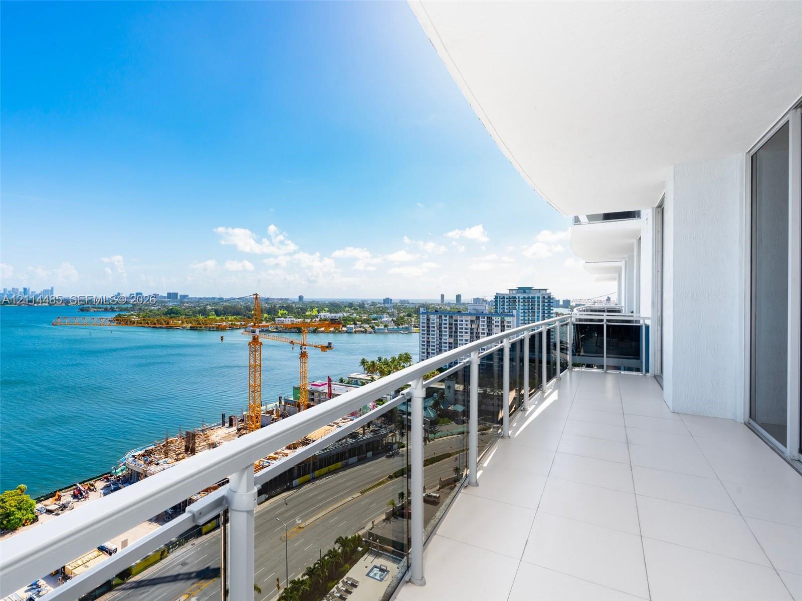 Covered balcony featuring white tile flooring, glass and metal railing, and expansive water backdrop