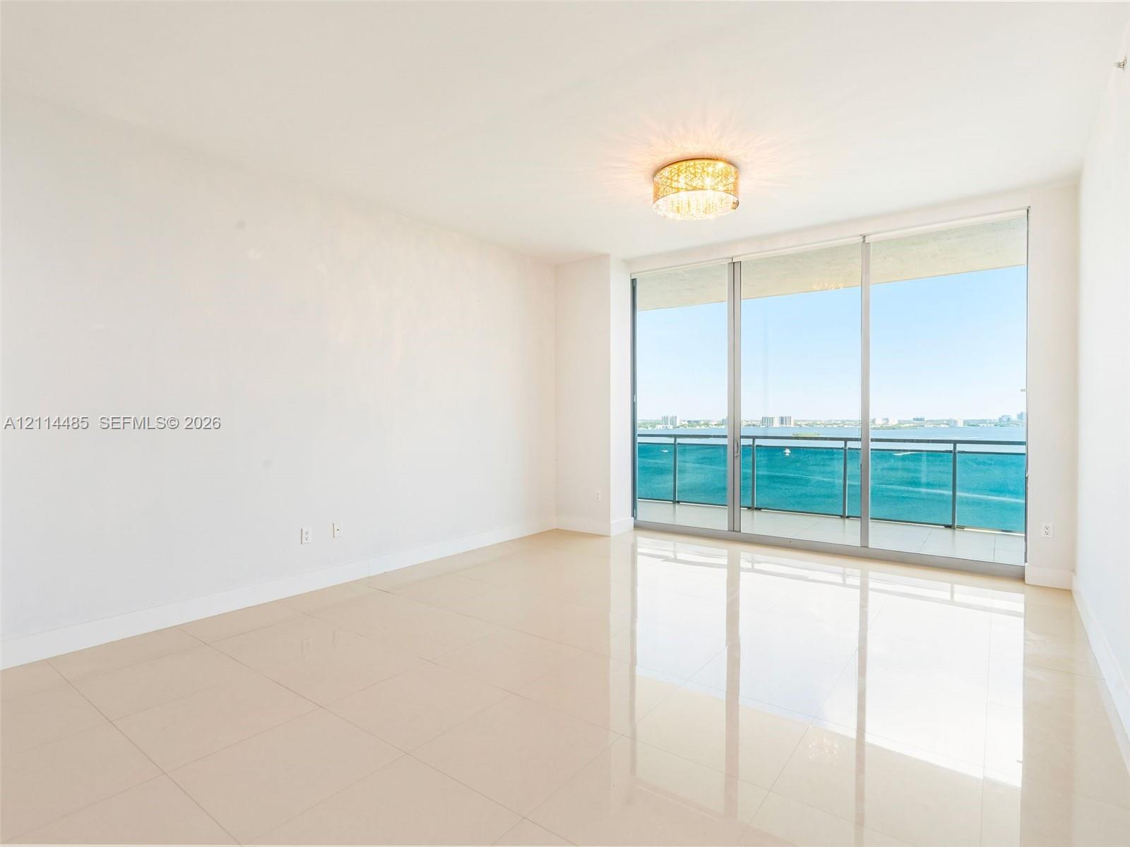 Floor-to-ceiling sliding glass doors, balcony with glass railing, polished tile flooring, and decorative flush-mount ceiling light fixture