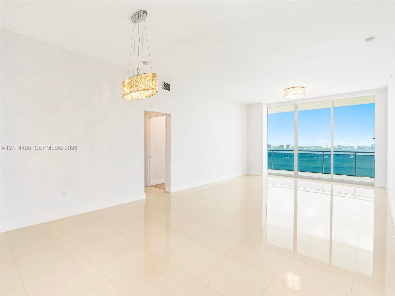 Open-concept room featuring polished tile flooring, floor-to-ceiling glass windows, a balcony with a glass railing, and decorative pendant lighting