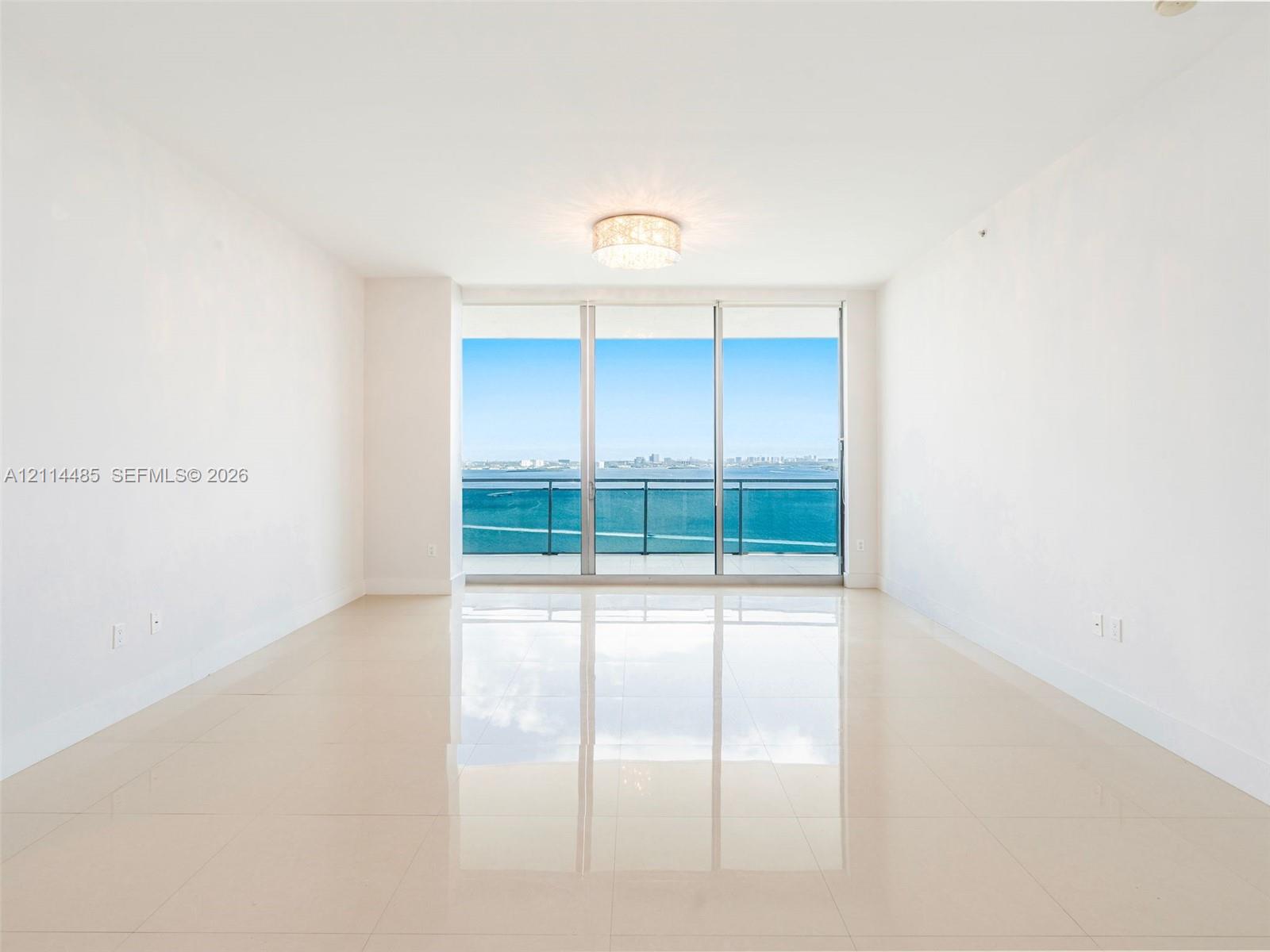 Floor-to-ceiling glass sliding doors, private balcony with metal railing, reflective tile flooring, and flush-mount crystal chandelier